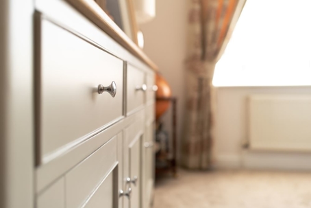 Shallow focus of a metal drawer knob seen on wooden sideboard furniture
